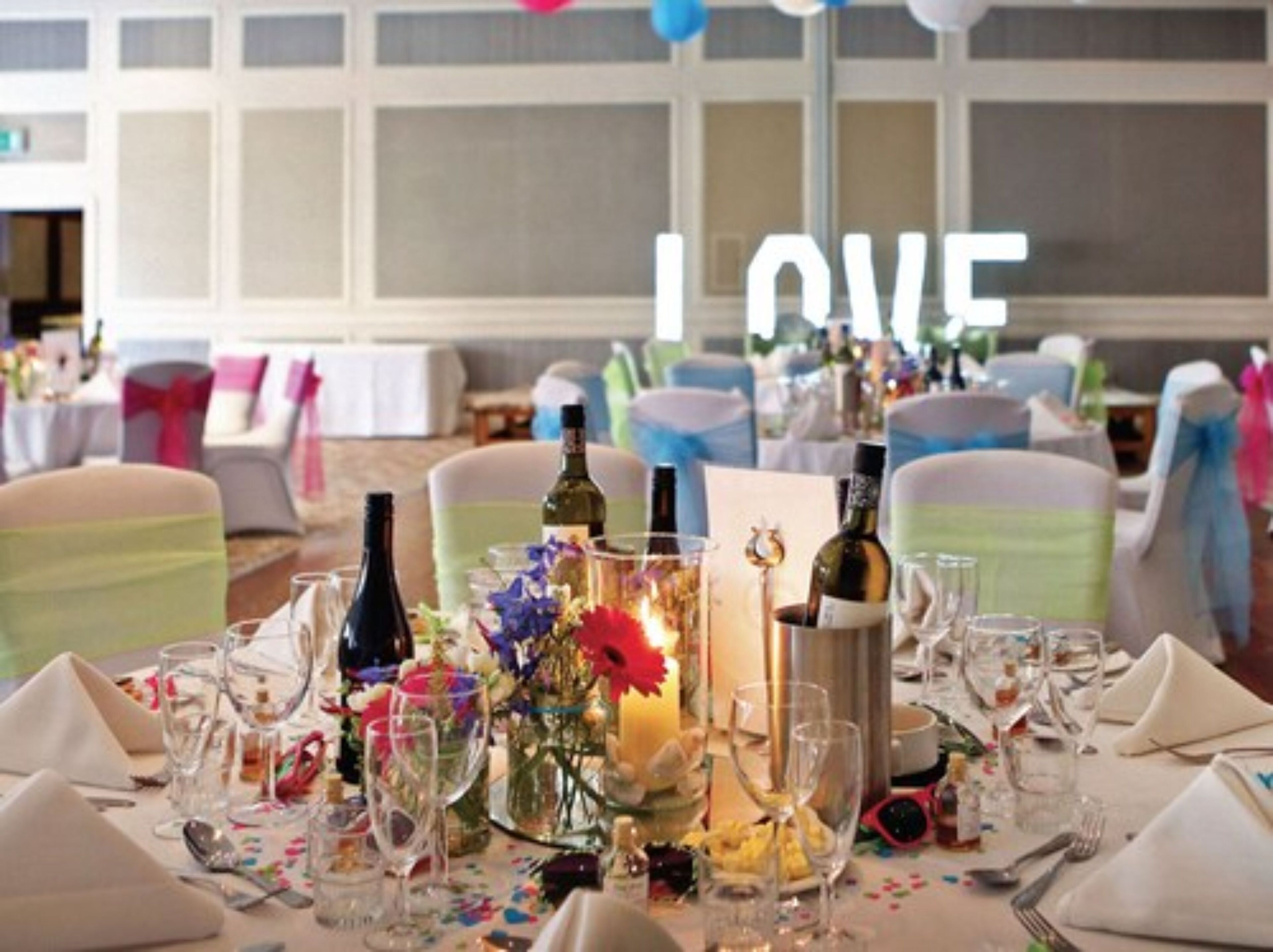 Une table de banquet dressée pour un événement formel, avec de nombreuses bouteilles de vin, des verres et un centre de table composé d’une bougie.