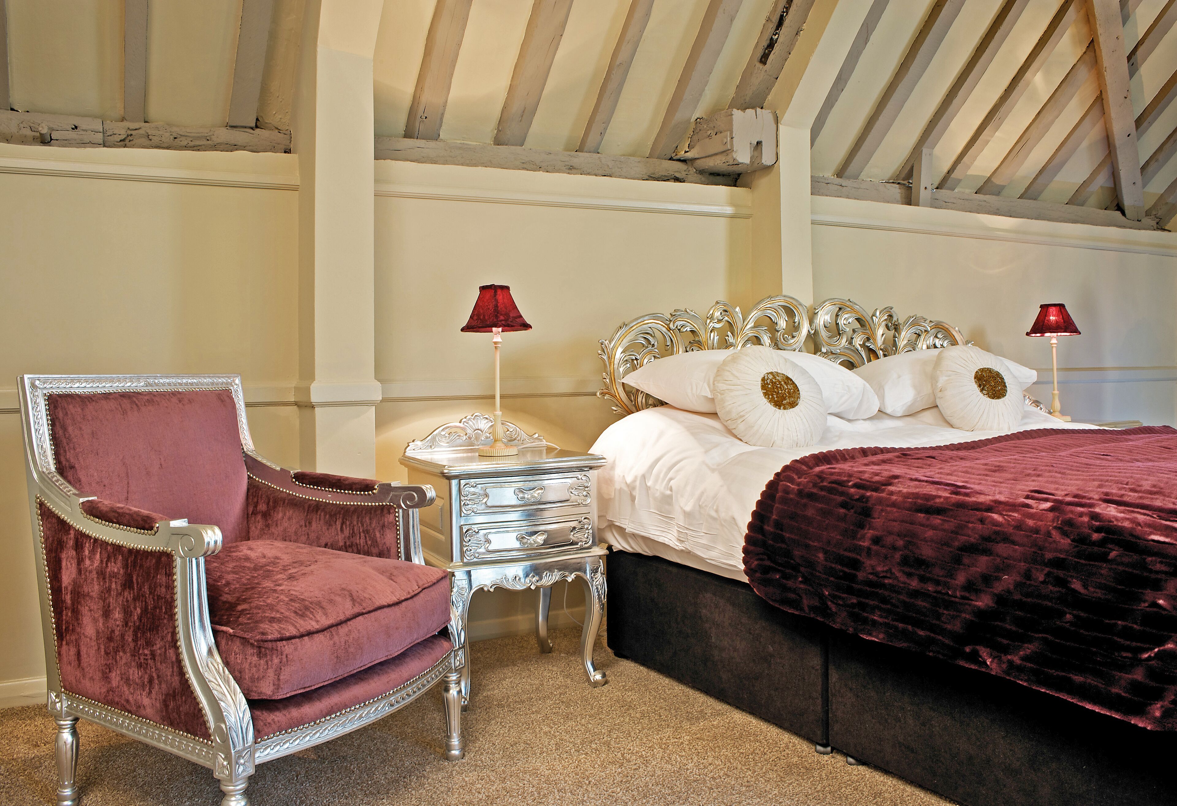 A bedroom with a large bed, a red lamp, a chair, and a nightstand.
