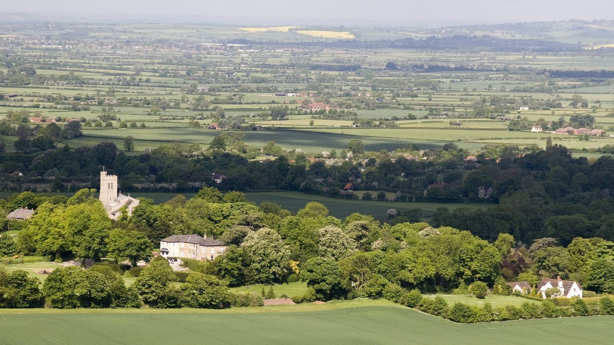 Un paisaje rural con una iglesia destacada y edificios residenciales en medio de campos verdes.