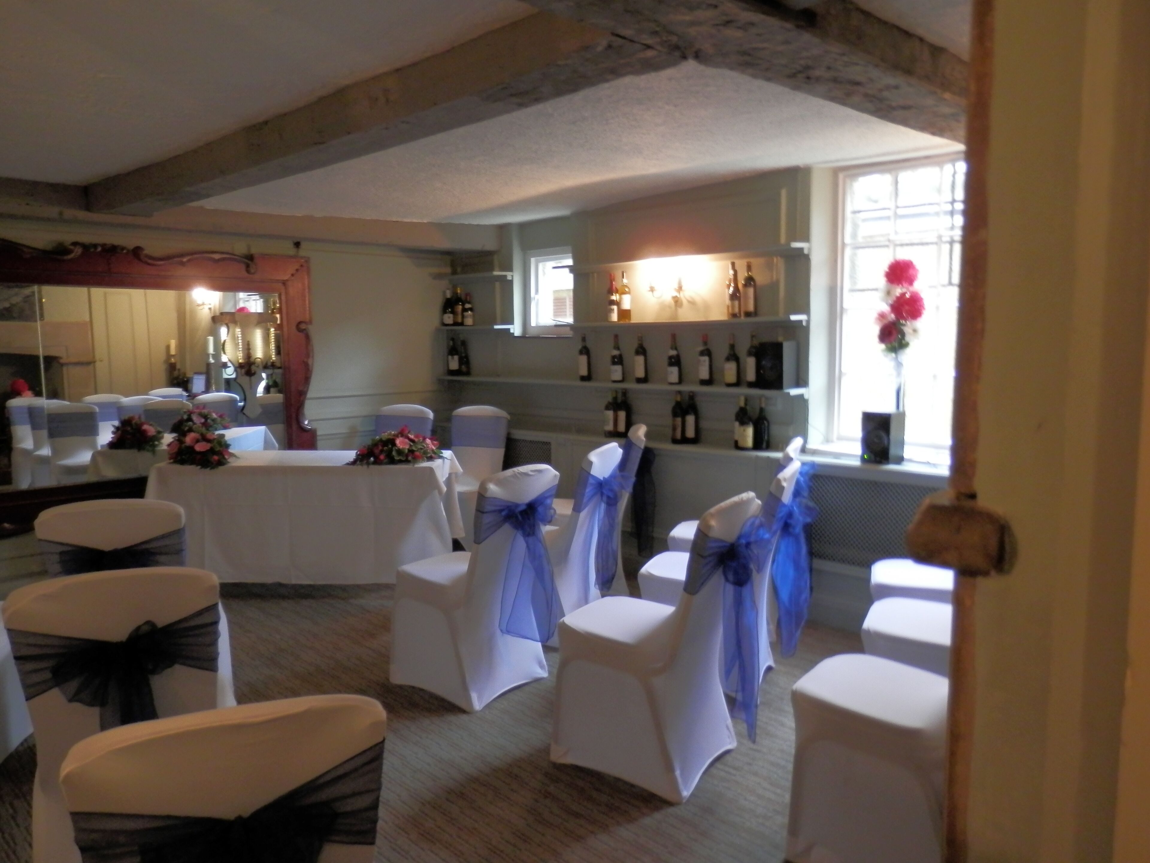 A banquet hall with white chairs and tables, a wine display, and a rustic ceiling.