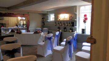 A banquet hall with white chairs and tables, a wine display, and a rustic ceiling.