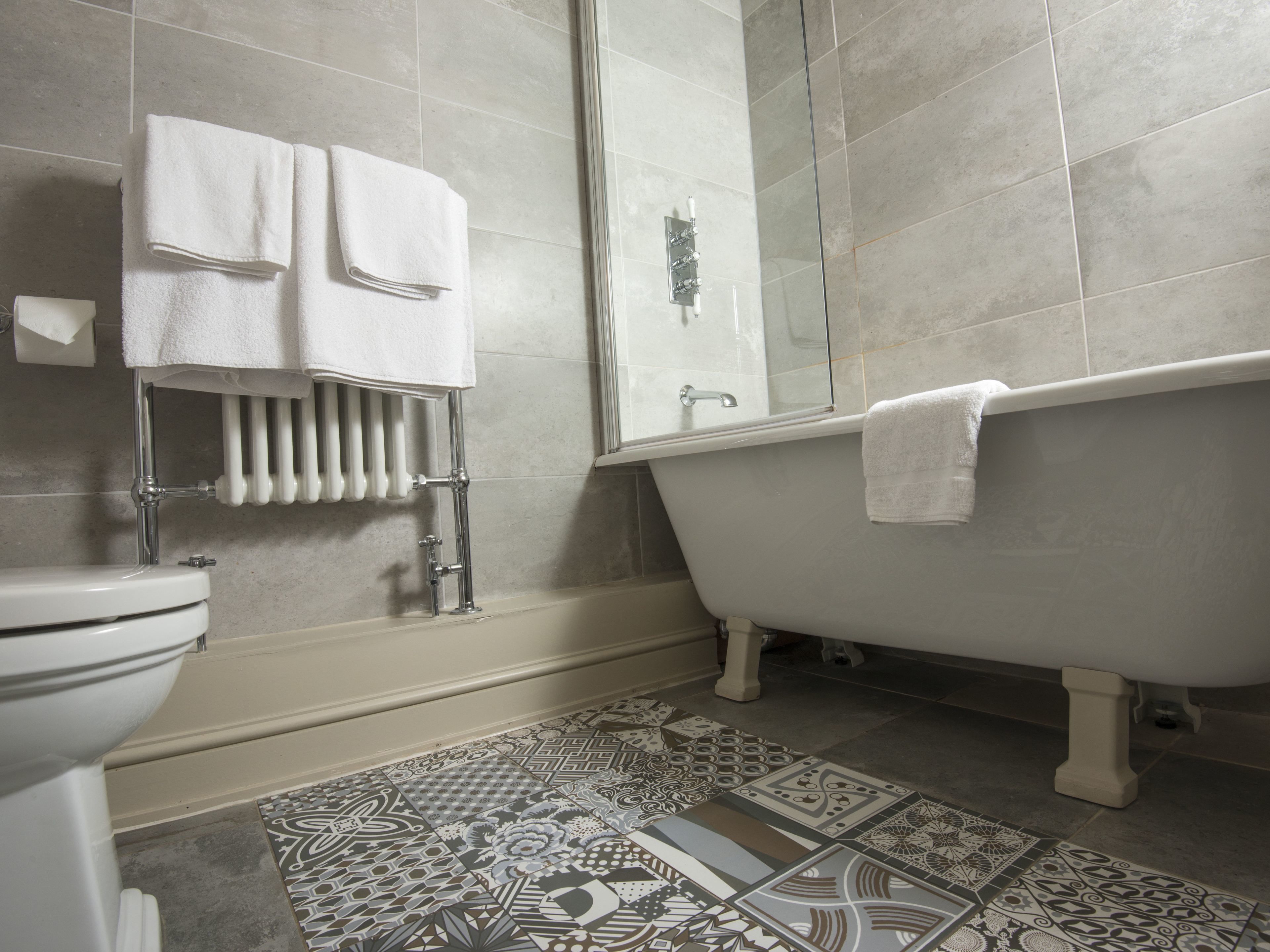 A bathroom with a toilet, a bathtub with a towel, a shower, and patterned floor tiles.