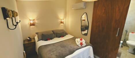 A bedroom with a bed, bedside lamps, a mirror, and a wooden door.