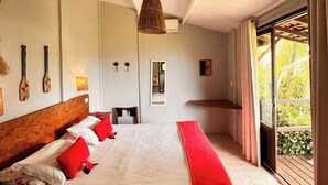 A bedroom with a large bed, a hanging light fixture, a window with curtains, and a view of greenery outside. - Pousada Ilha do Frade (Fernando de Noronha)