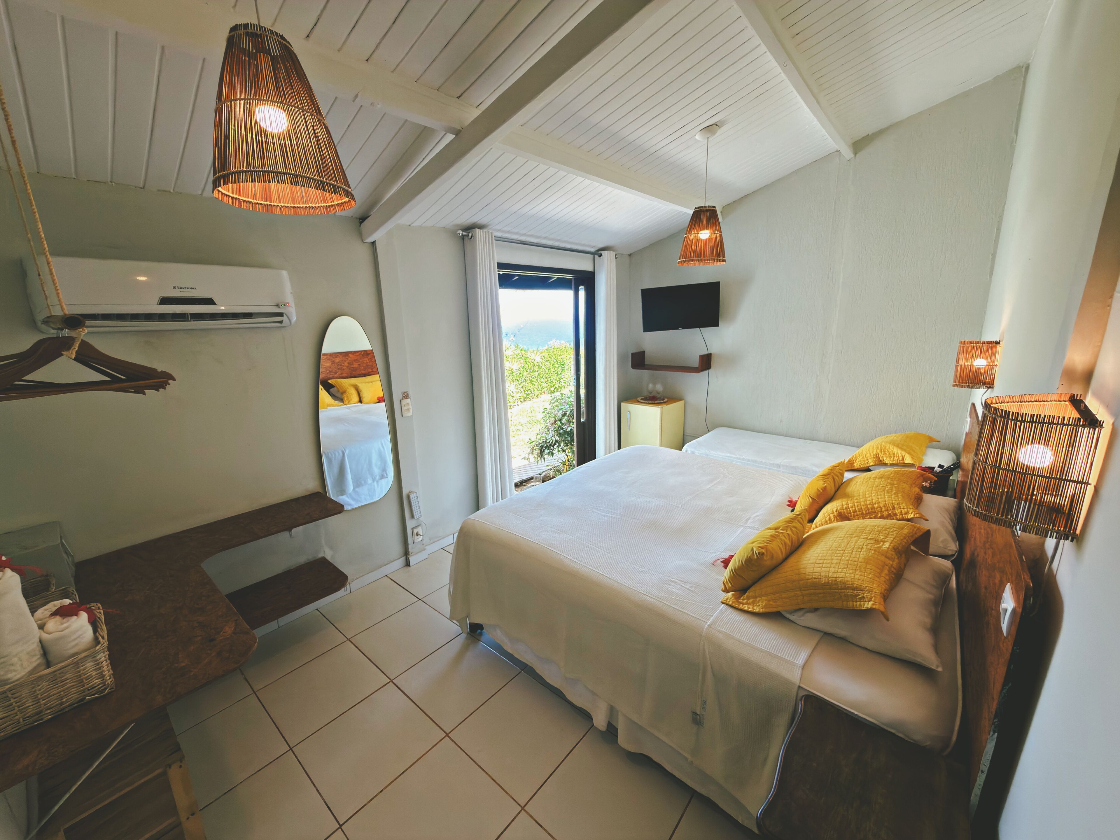Quarto com cama, abajures, televisão, espelho e janela.