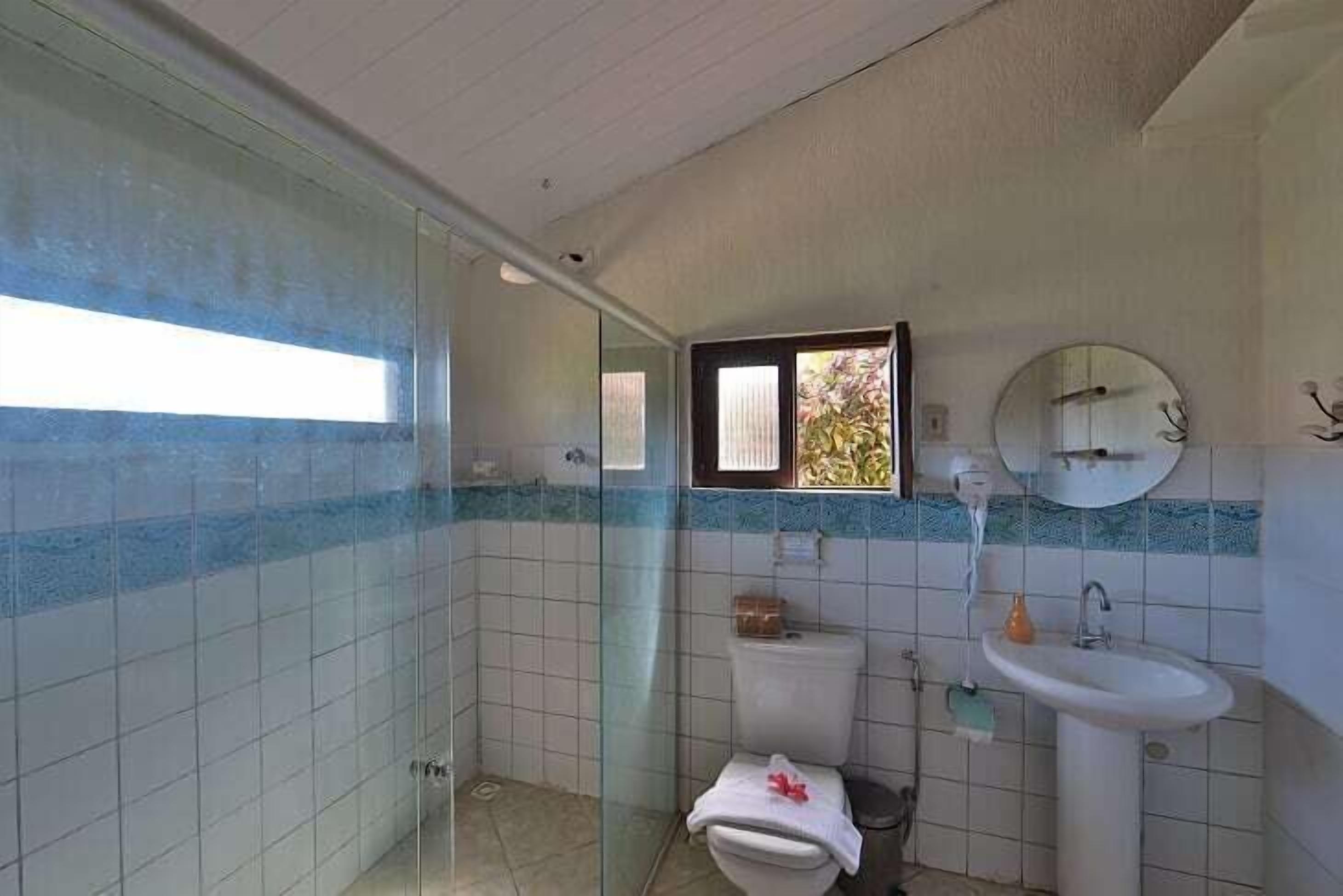 Un baño con cabina de ducha de vidrio, inodoro, lavabo y ventana.