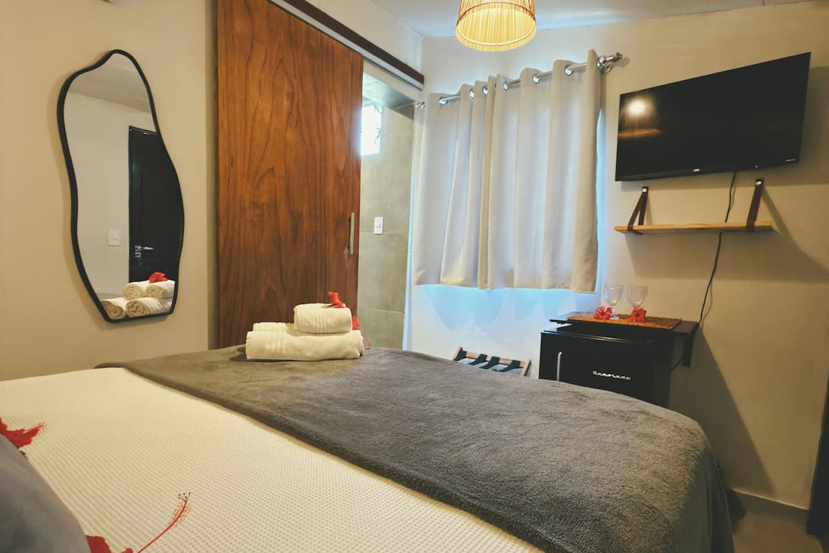 Quarto de hotel com uma cama grande, televisão fixada na parede e guarda-roupa de madeira.