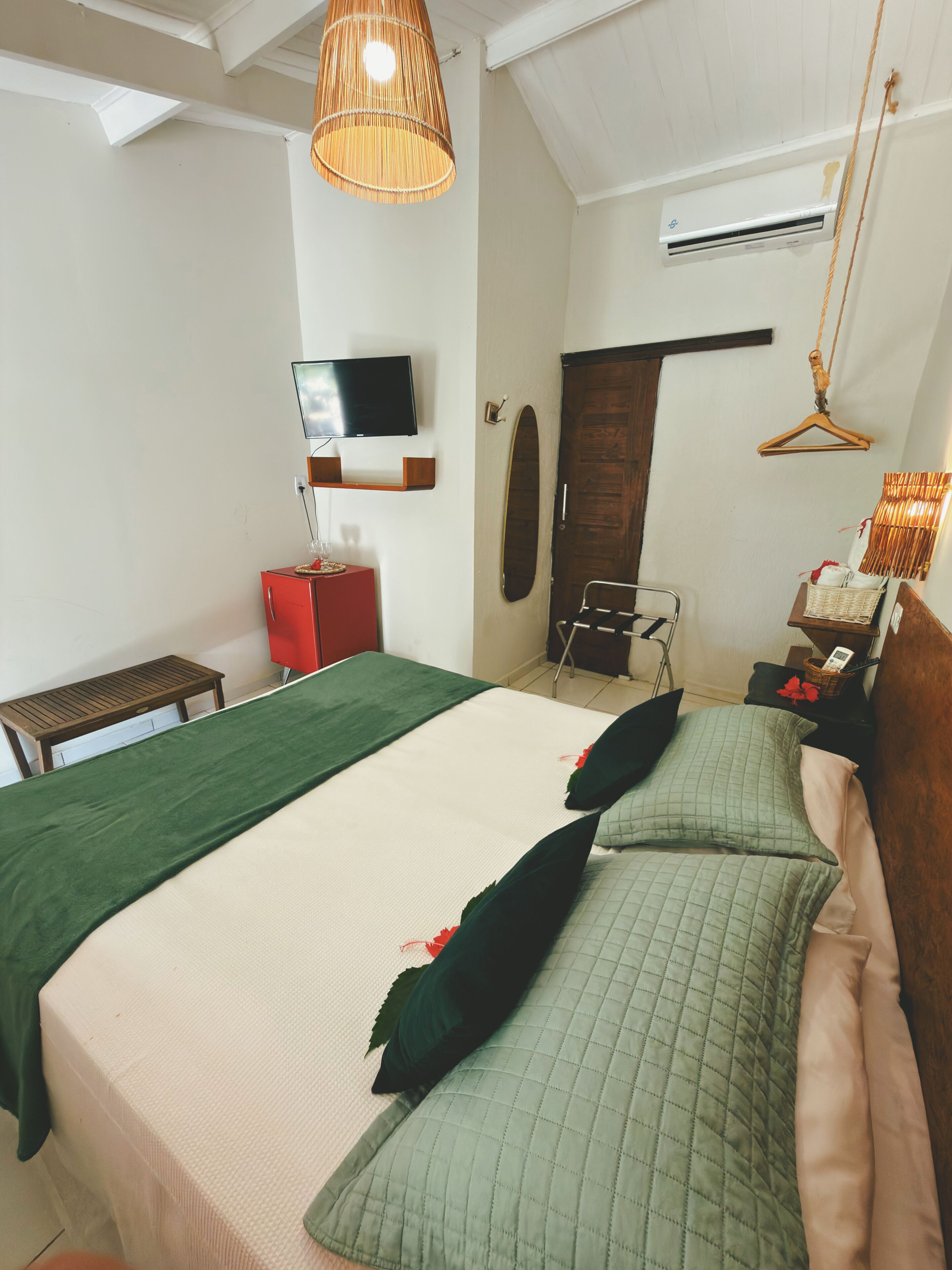Quarto com cama, televisão, ar-condicionado, luminária pendente e porta de madeira.