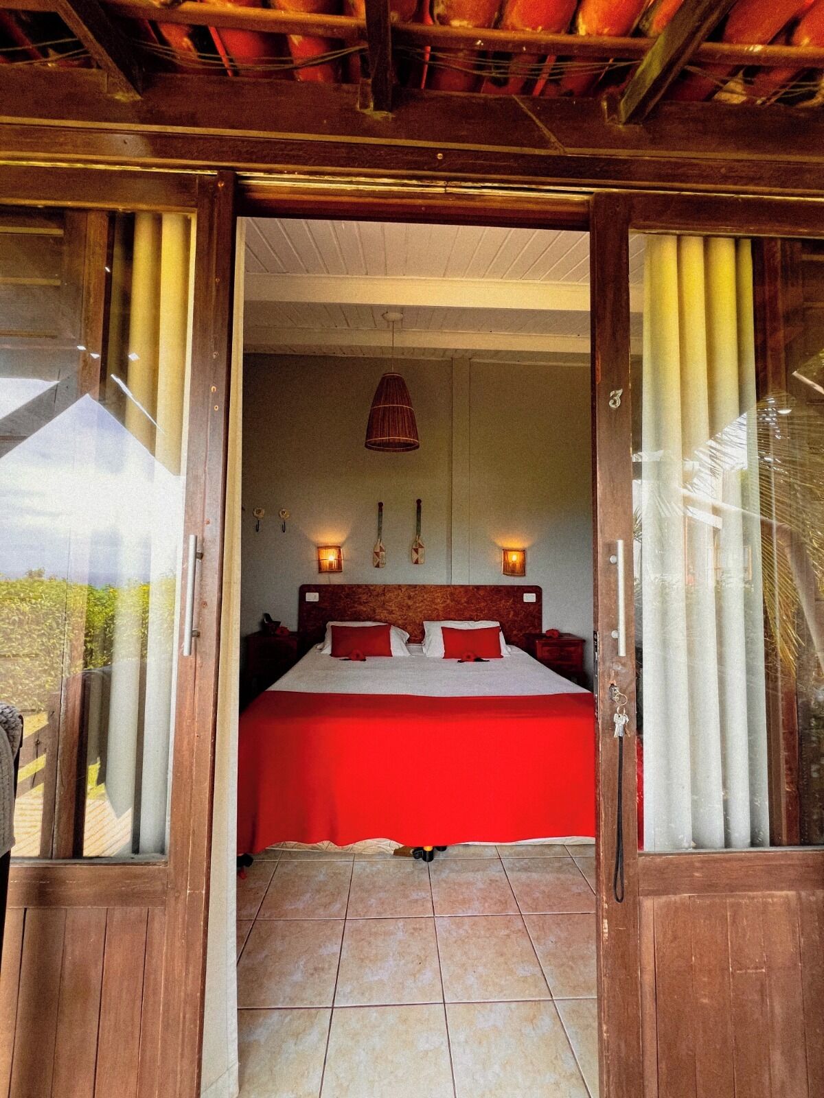 Un dormitorio con una colcha roja, cabecera de madera y una lámpara colgante.