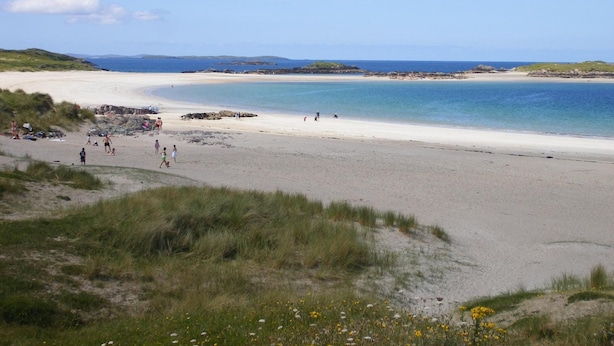 A beach with people walking and sitting, a clear sky, and distant hills. - Camillaun Lodge (Oughterard)