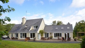 A two-story house with a patio area, large windows, and a chimney. - Camillaun Lodge (Oughterard)