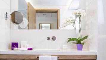 Un baño moderno con un tocador blanco, un gabinete de madera, un espejo, una orquídea en maceta y una toalla sobre la encimera.