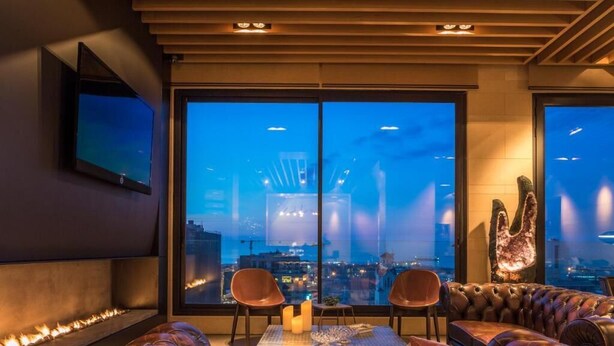 A modern lounge with leather seating, a fireplace, and a large window offering a city view. - O Monot Hotel (Beirut)