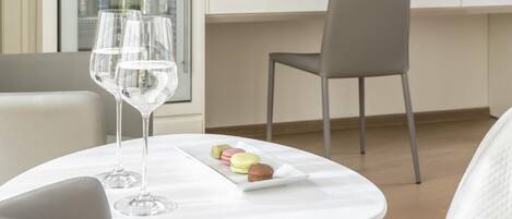 Ein modernes Hotelzimmer mit weißem Schreibtisch, Flachbildfernseher, Lampe und einem Glas Wein auf einem kleinen Tisch.