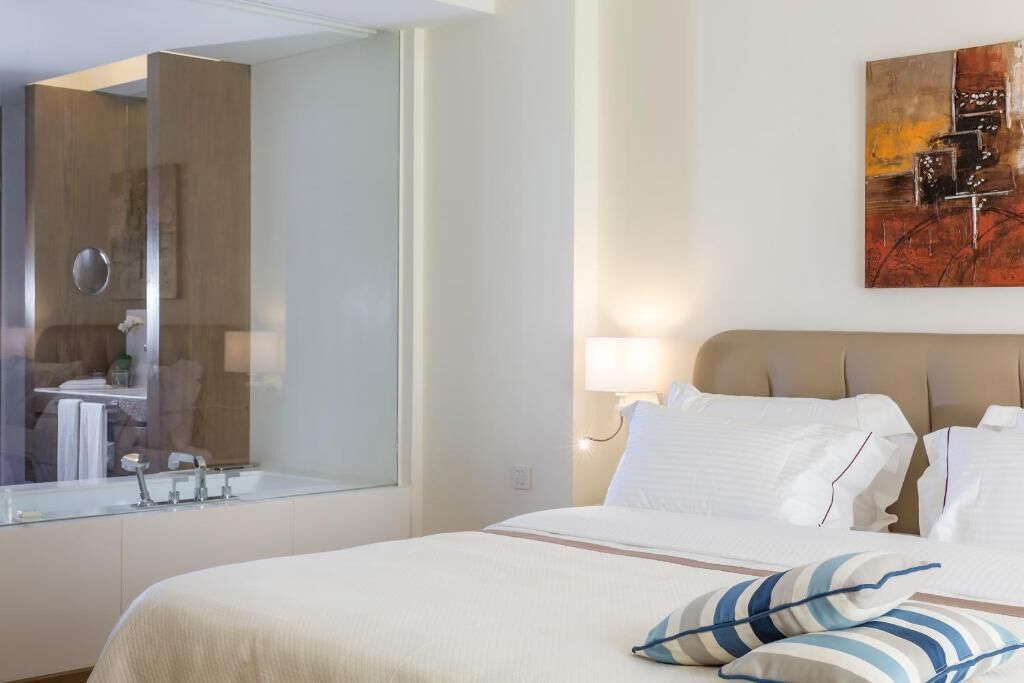 Une chambre d’hôtel avec un grand lit, un miroir, un tableau accroché au mur et une salle de bain visible dans le reflet du miroir.