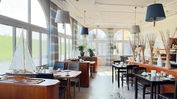 Un vaste espace dédié à la salle à manger, doté de hauts plafonds, de grandes fenêtres et d’un éclairage moderne suspendu.