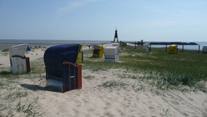 A beach with a lighthouse, sand, and beach chairs. - Seehotel Neue Liebe (Cuxhaven)