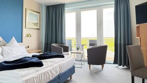 A hotel room with a bed, two armchairs, a desk, and a balcony with curtains. - Seehotel Neue Liebe (Cuxhaven)
