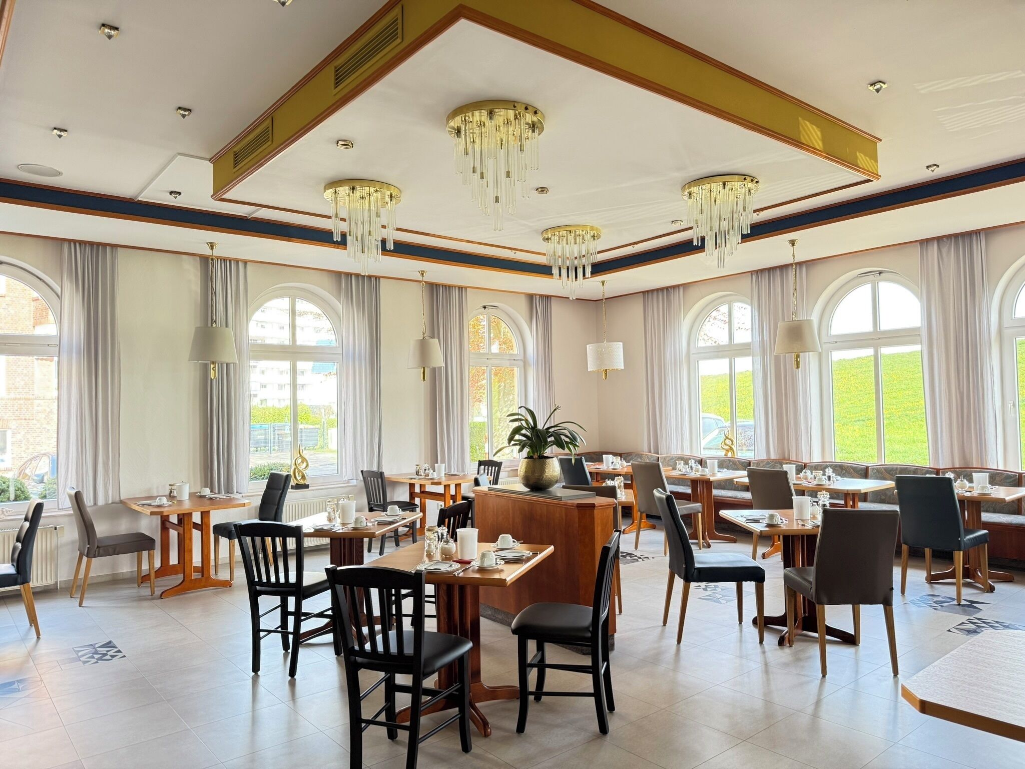 Un comedor amplio con varias mesas y sillas, ventanas grandes y candelabros.