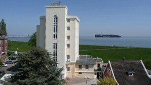 A hotel with a view of the water and a ship in the distance. - Seehotel Neue Liebe (Cuxhaven)