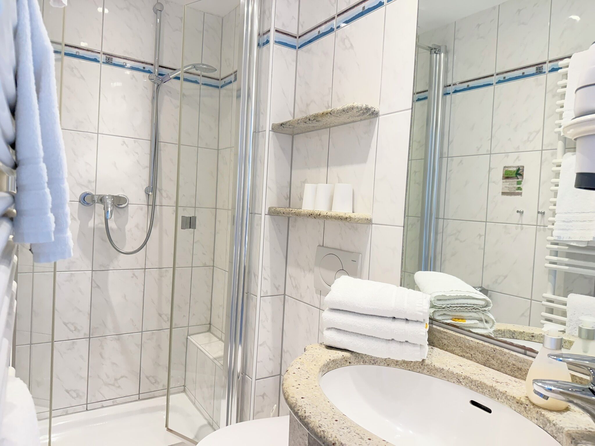 Ein modernes Badezimmer mit einer gläsernen Duschkabine, einem Waschbecken mit Granitplatte und einem Spiegel mit Handtuchhalter.