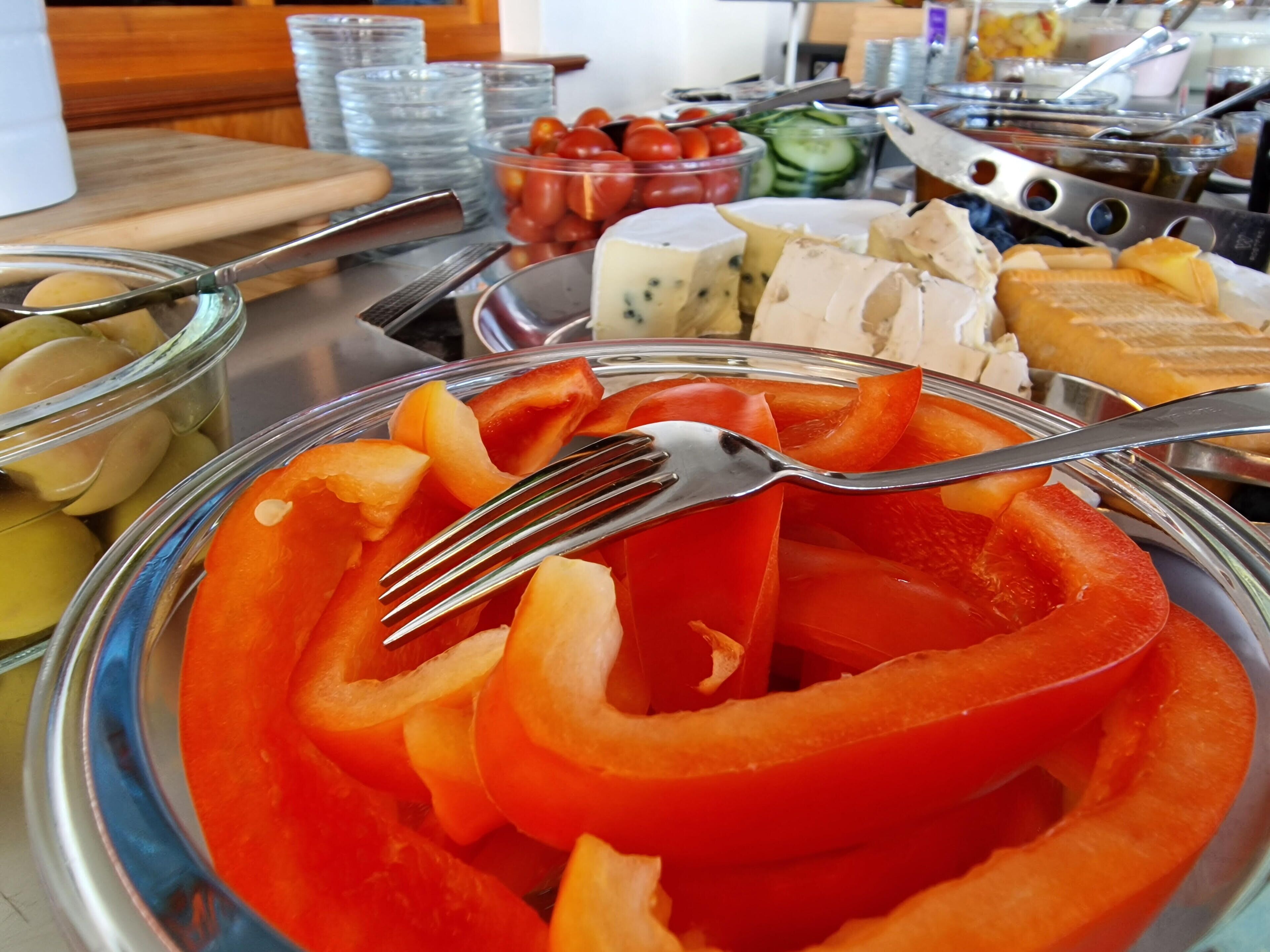 Una mesa de buffet con diversos alimentos, incluyendo pimientos rojos en rodajas, queso y otros platos preparados.