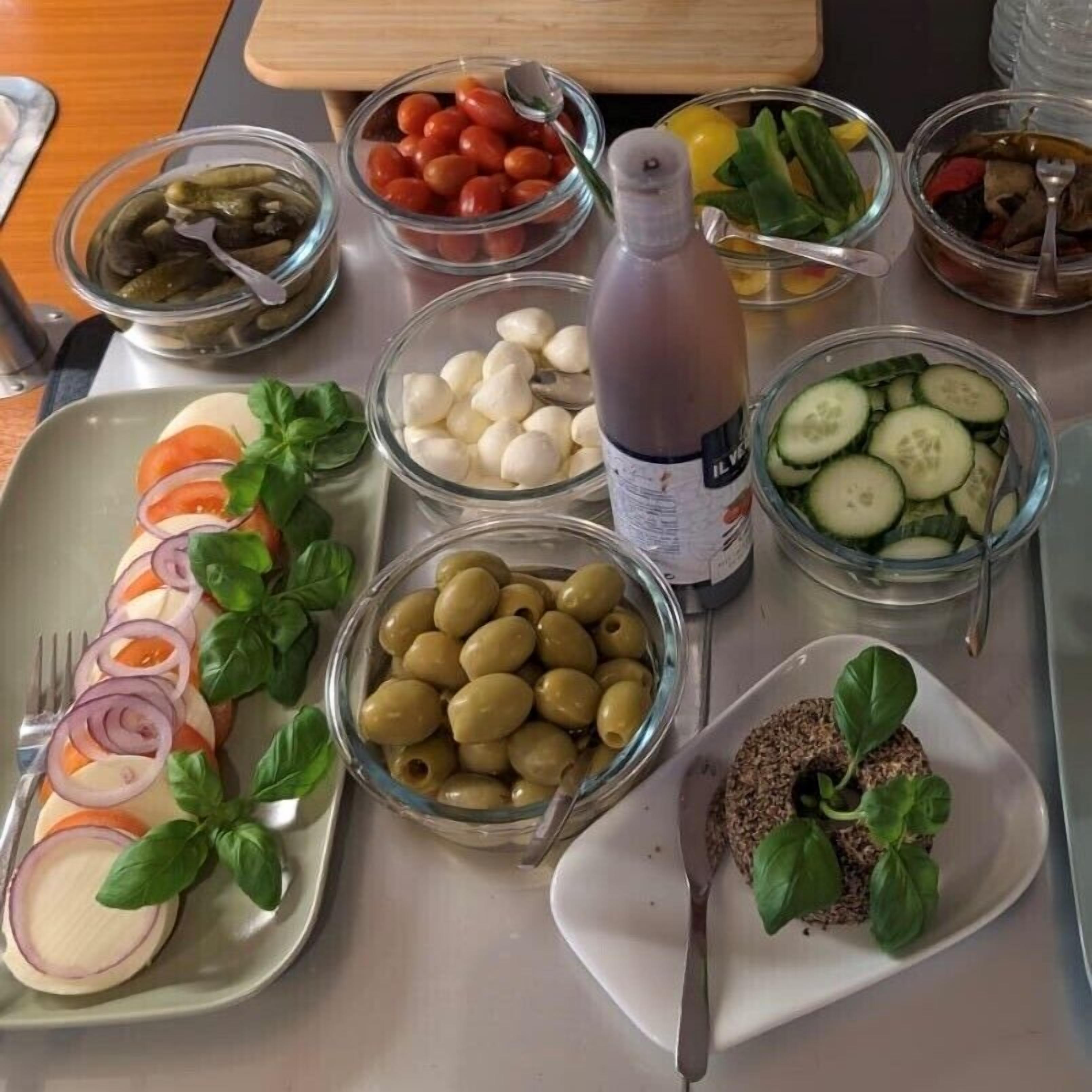 A table with various food items including olives, tomatoes, cucumbers, and a bottle of dressing.