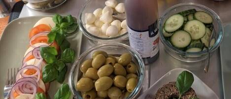 Ein Tisch mit verschiedenen Speisen, darunter Oliven, Tomaten, Gurken und einer Dressingflasche.