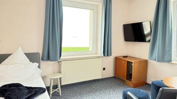 A hotel room with a bed, a small stool, a wooden cabinet, a TV, and a window with curtains.