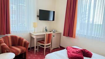 Ein Hotelzimmer mit einem Bett, einem Schreibtisch mit Stuhl, einem Fernseher und einem Fenster mit Vorhängen.