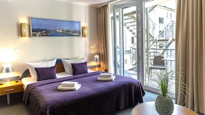 A hotel room with a bed, two bedside tables, a window with a view of a cityscape, and a potted plant. - Hotel Ambiente Berlin City (Berlin)