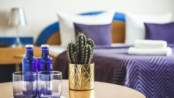 A bed with a purple and white bedspread, a gold decorative vase with a cactus, and two blue bottles on a table.