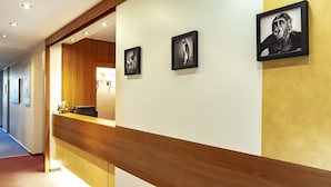 A reception area with a wooden reception desk, framed artwork on the wall, and a hallway leading to other rooms. - Hotel Ambiente Berlin City (Berlin)