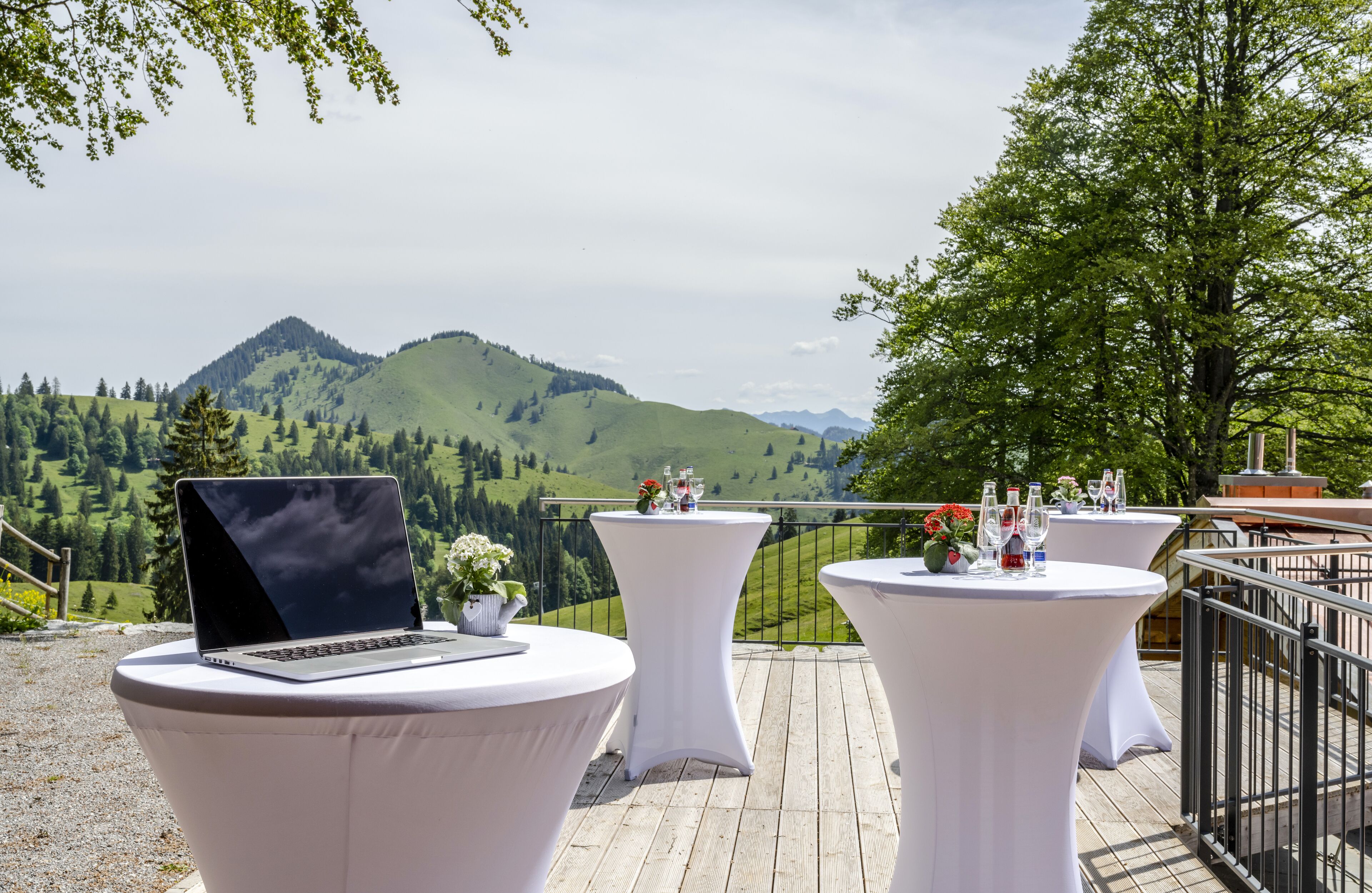 A terrace with round tables, a laptop, and a scenic mountain view.