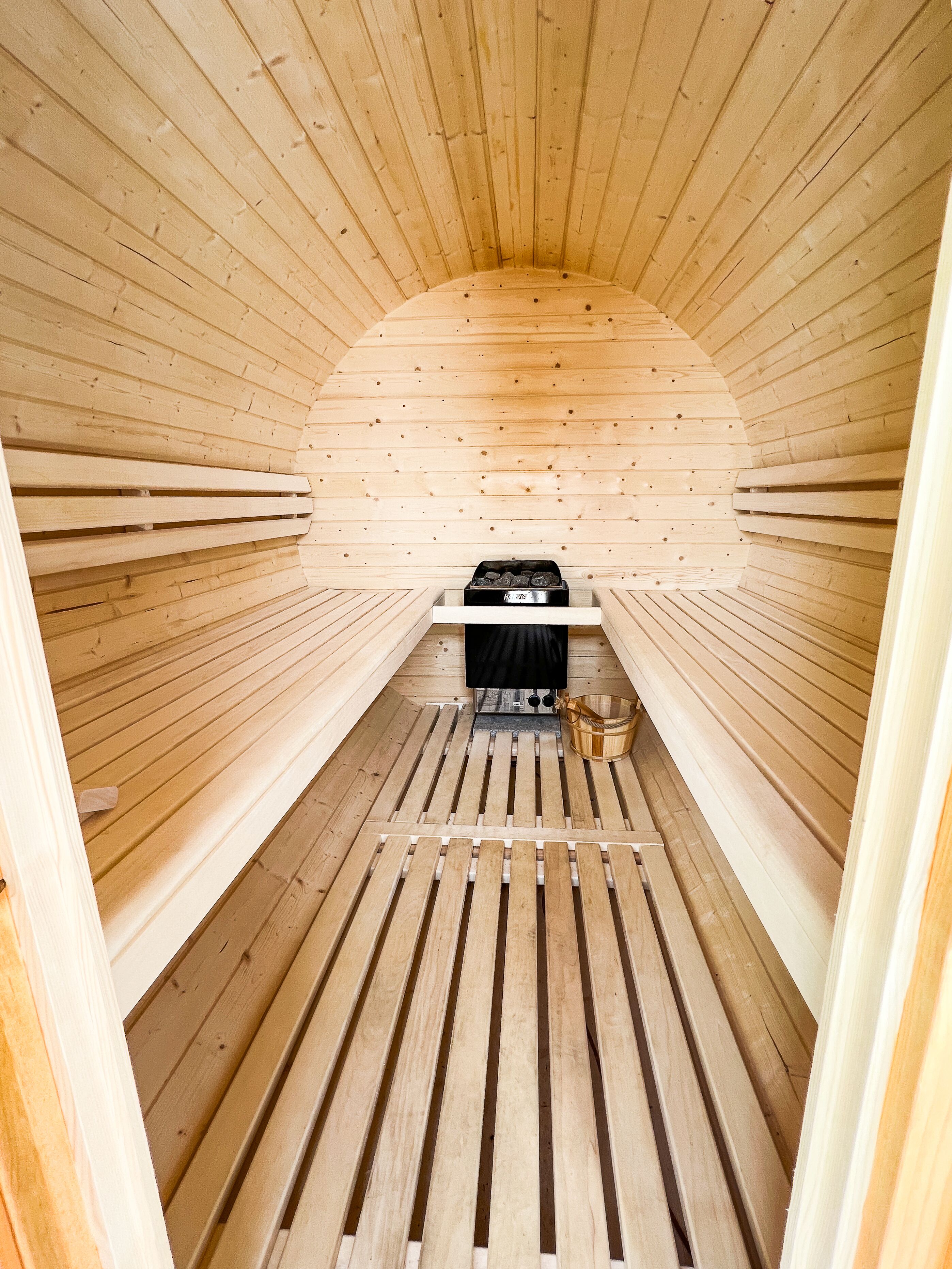 Een sauna met houten latten op de wanden en de vloer, een bank en een sauna-oven.