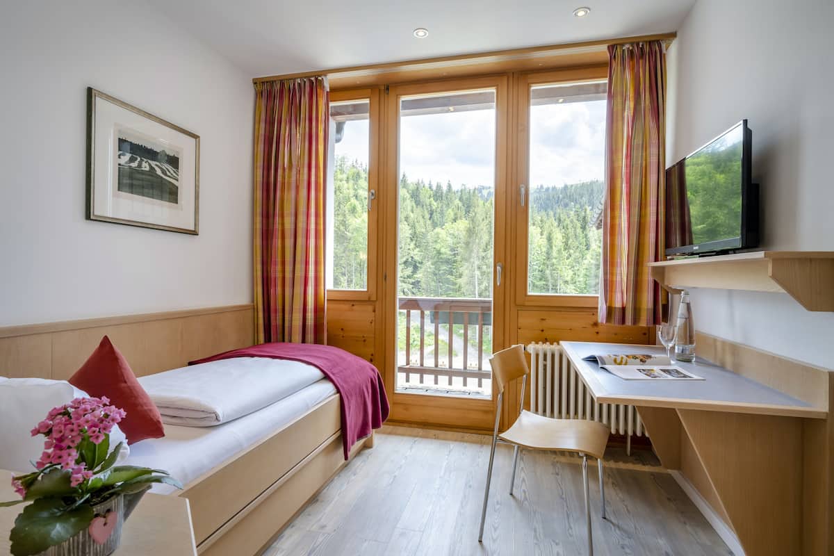 Een kleine kamer met een bed, een bureau, een stoel en een televisie.