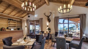 Un restaurante con techos de madera, candelabros y una cabeza de venado montada en la pared. Las mesas están dispuestas para comer, con sillas.