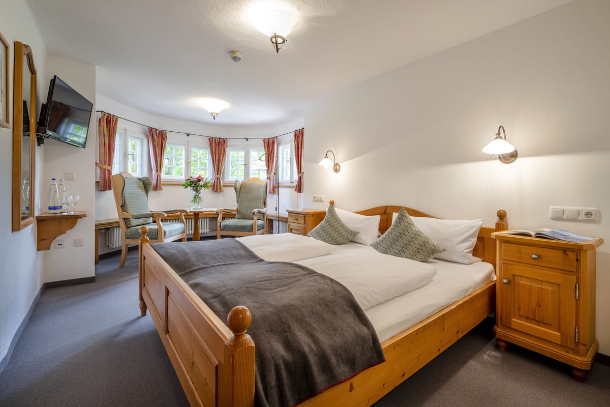 Een goed verlichte slaapkamer met een houten bed, nachtkastjes, een televisie en een bureau met een stoel.
