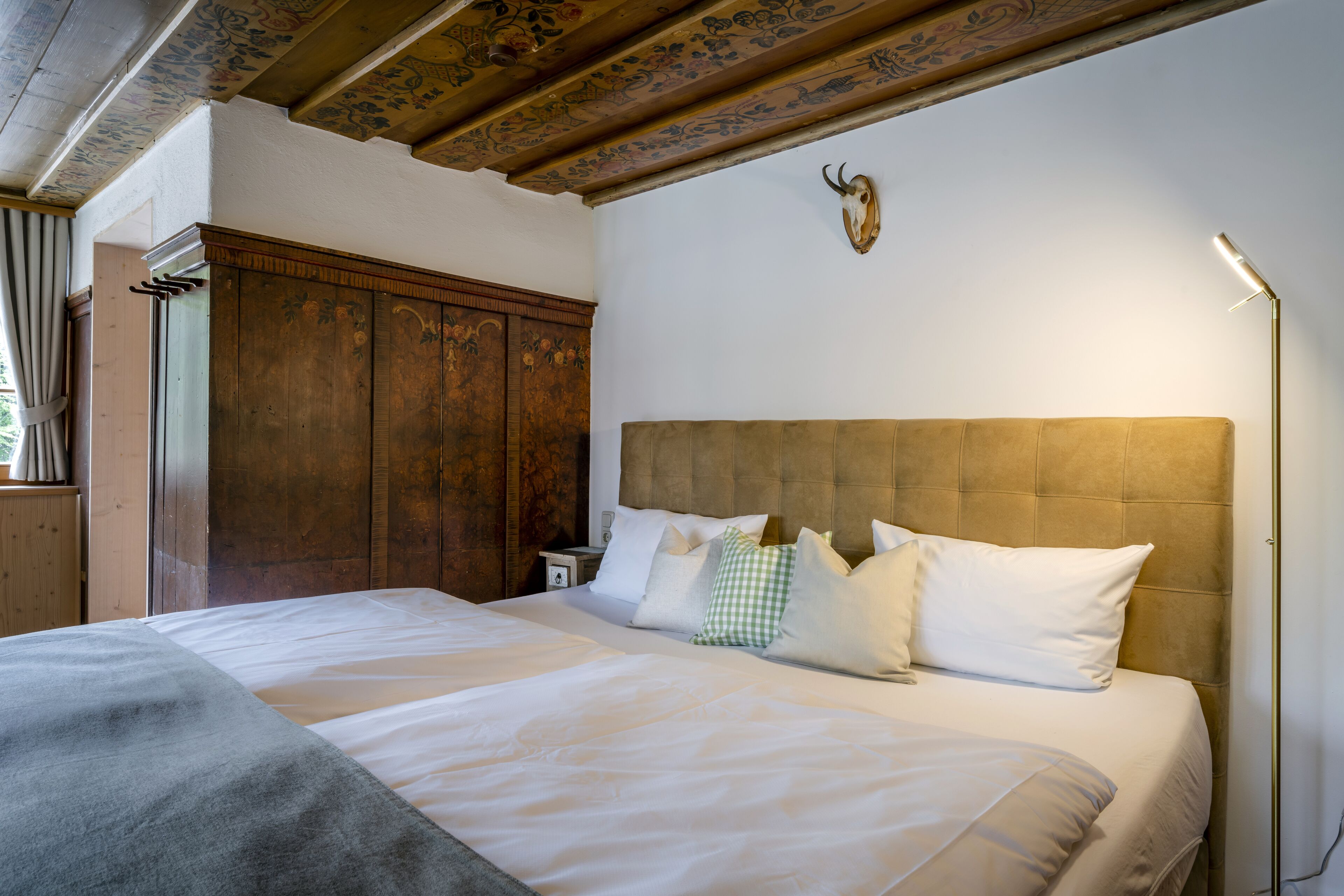 Un letto rifatto con cuscini bianchi e verdi a quadretti, un armadio in legno e una testa di animale appesa al muro.
