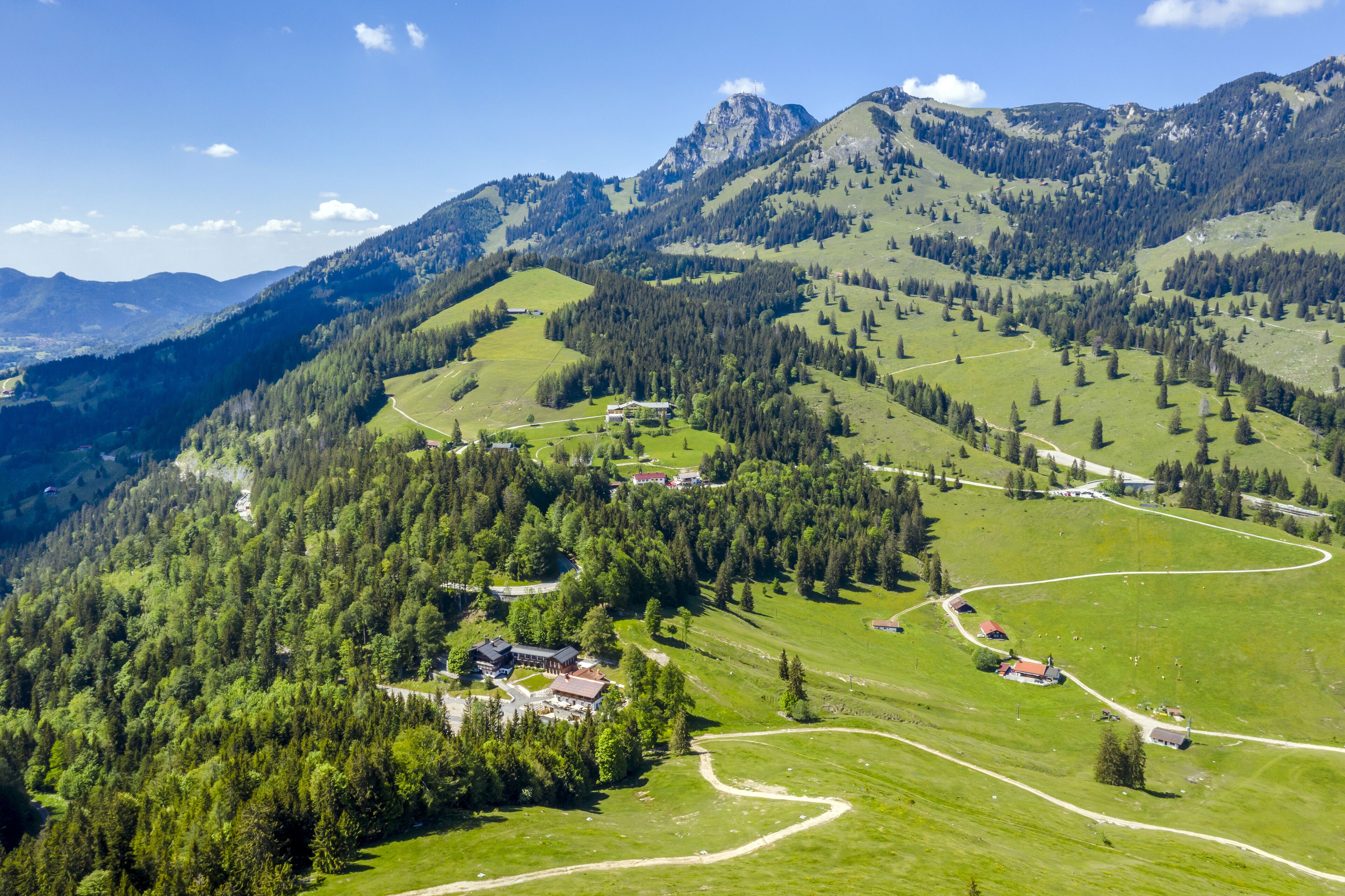 A mountainous landscape with a winding road, several buildings, and dense forests.