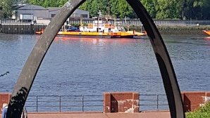 A waterfront view with a metal arch structure, a bird feeder, and a dock with boats. - Hotel Havenhaus (Bremen)
