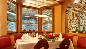 A dining area with a table set for two, red cushioned booths, and large windows with decorative glass panes. - Hotel Wo Der Hahn Kräht (Flein)
