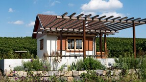 A small house with a wooden pergola, surrounded by a stone wall and a garden with various plants and flowers. - Hotel Wo Der Hahn Kräht (Flein)
