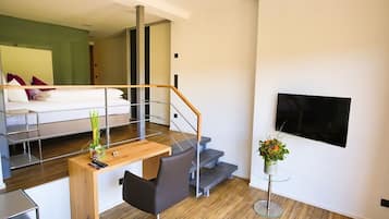 Una habitación de hotel moderna con un escritorio de madera, una silla, un televisor de pantalla plana montado en la pared y una escalera que conduce a un nivel superior.