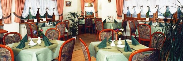 Un área de comedor con varias mesas preparadas para el servicio, sillas y una mesa central con una planta.