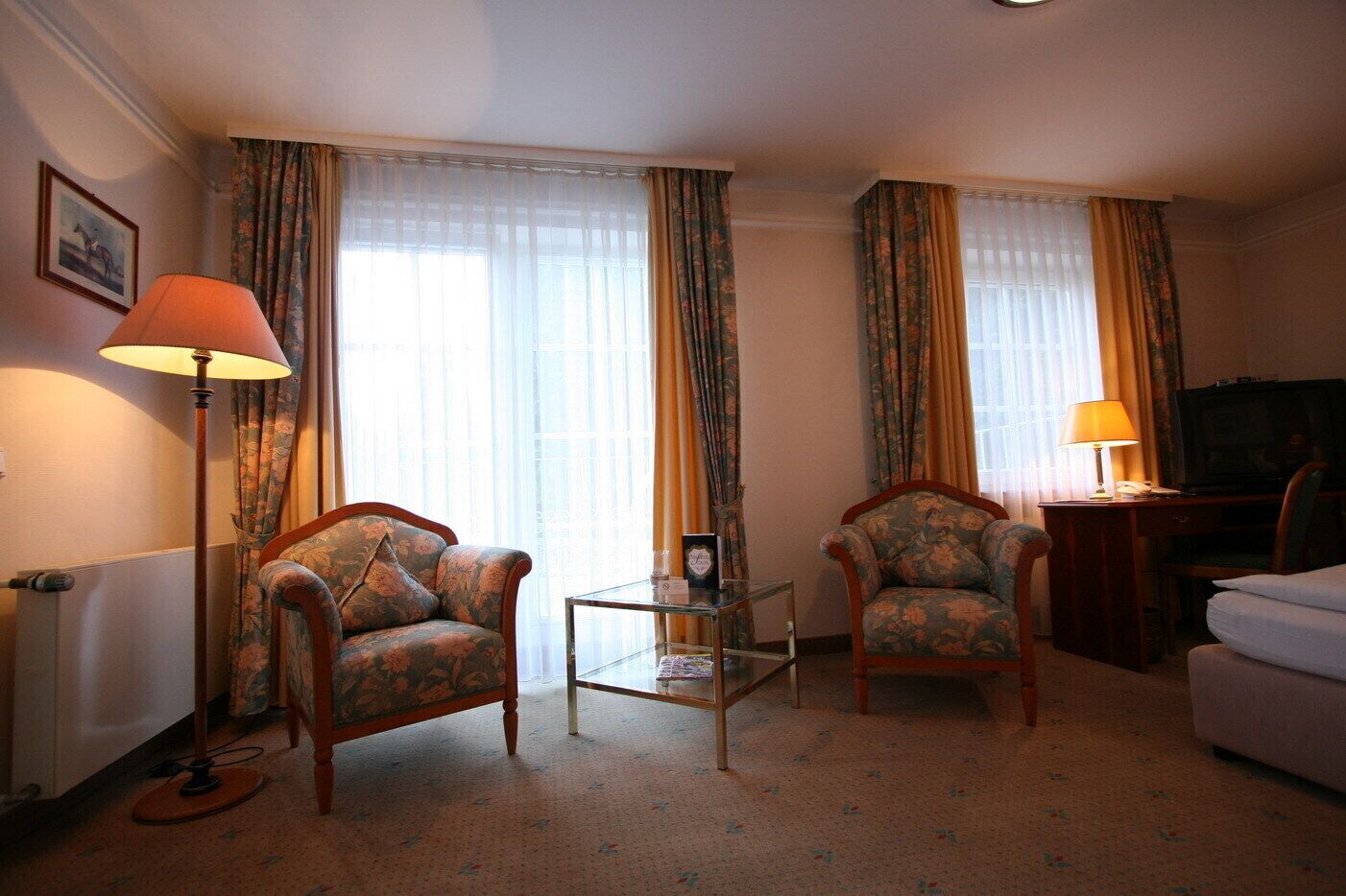 A hotel room with two armchairs, a small table, a sofa, a television, and a lamp.
