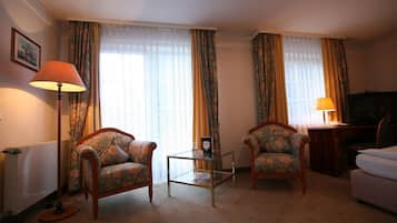 A hotel room with two armchairs, a small table, a sofa, a television, and a lamp.