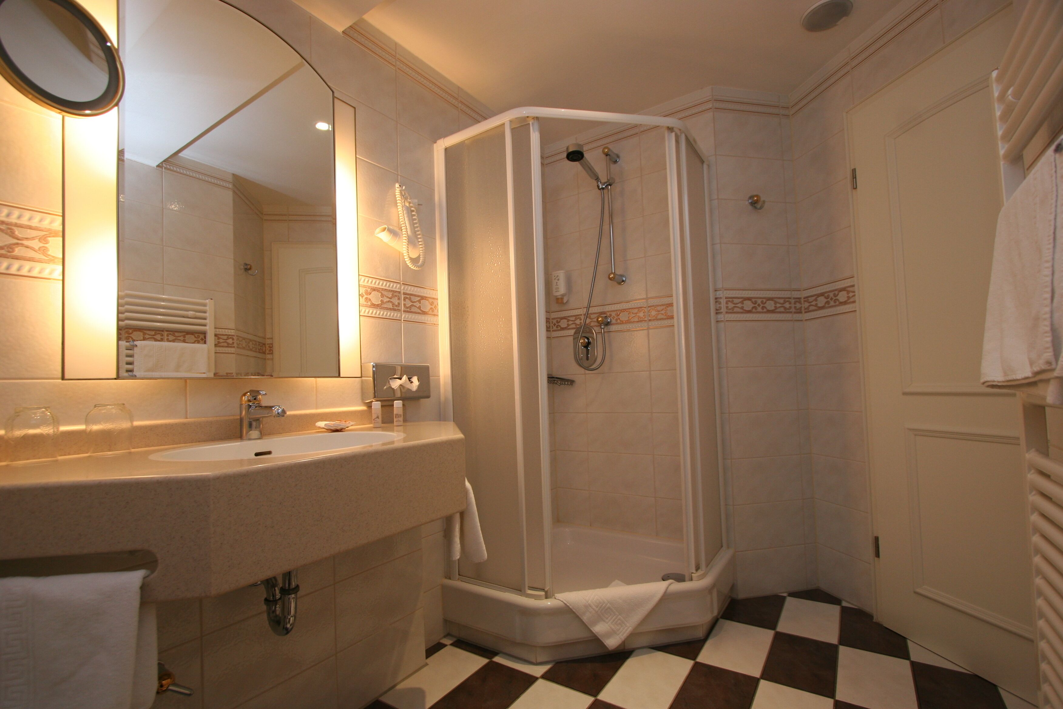 A bathroom with a sink, mirror, shower, and checkered floor.