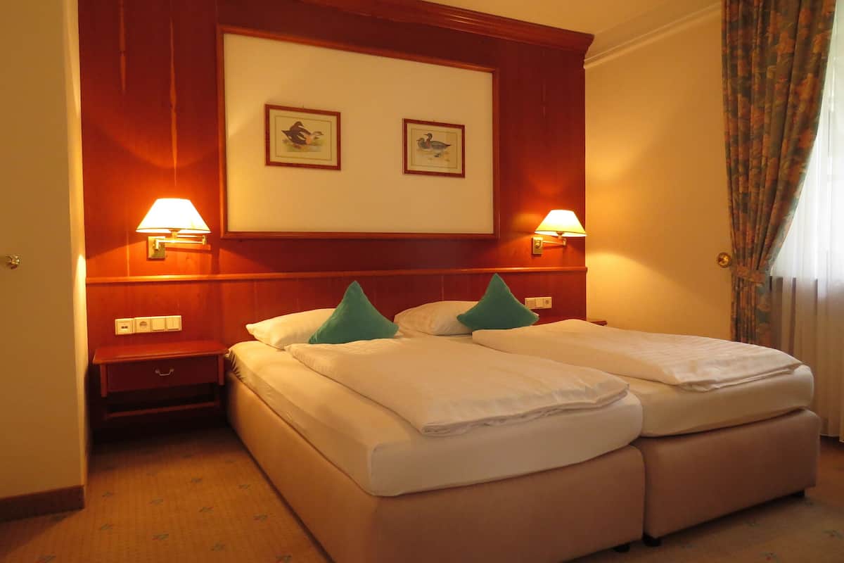 A hotel room with two beds, a wooden headboard, two wall-mounted lamps, and a framed picture above the beds.