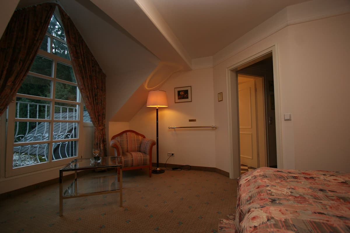 A bedroom with a bed, a chair, a table, a lamp, and a window with curtains.